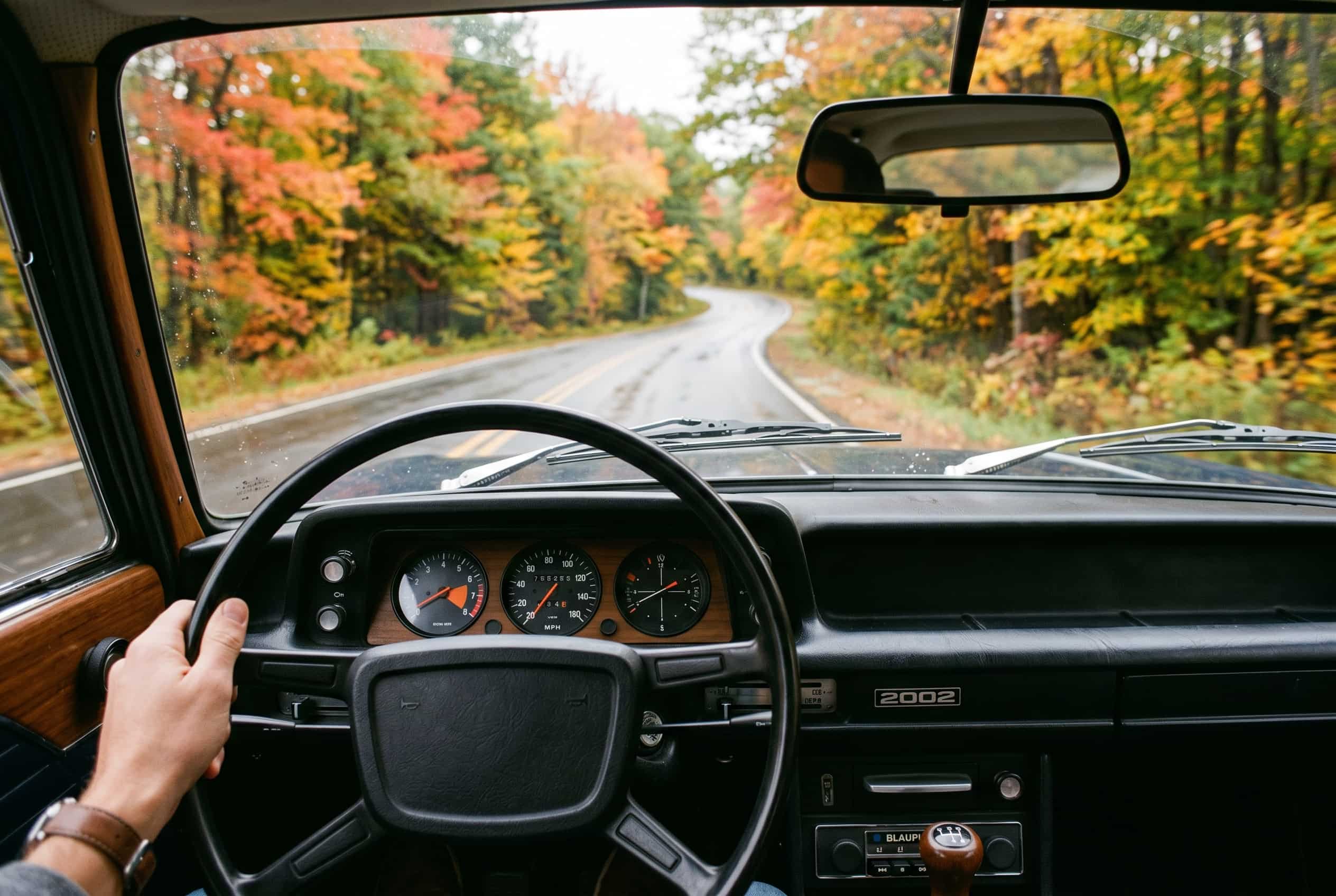 The thinking car – BMW 2002 driver's view Driver's-eye view of a 1970s BMW 2002 dashboard with simple instruments and a narrow road through autumn woods ahead