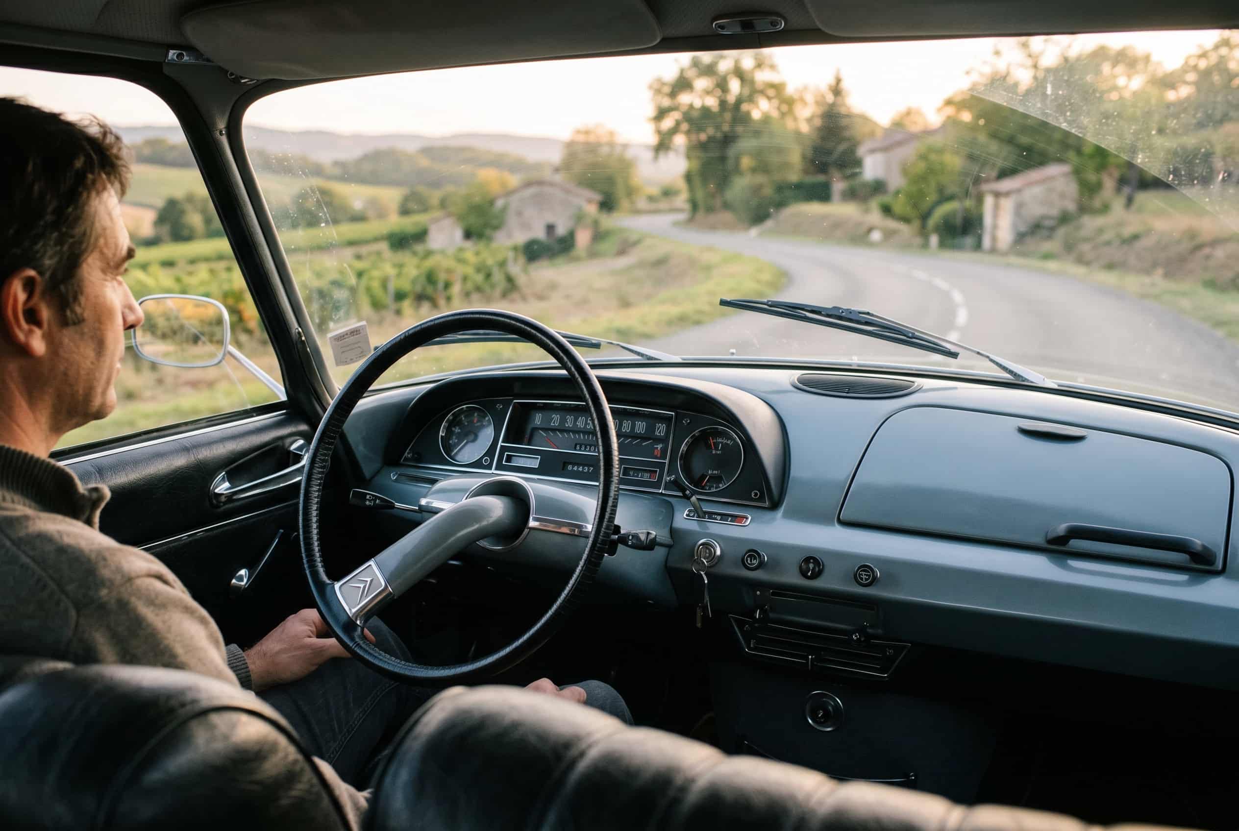 1960s Citroën DS dashboard with single-spoke steering wheel and minimal instruments, French country road visible outside