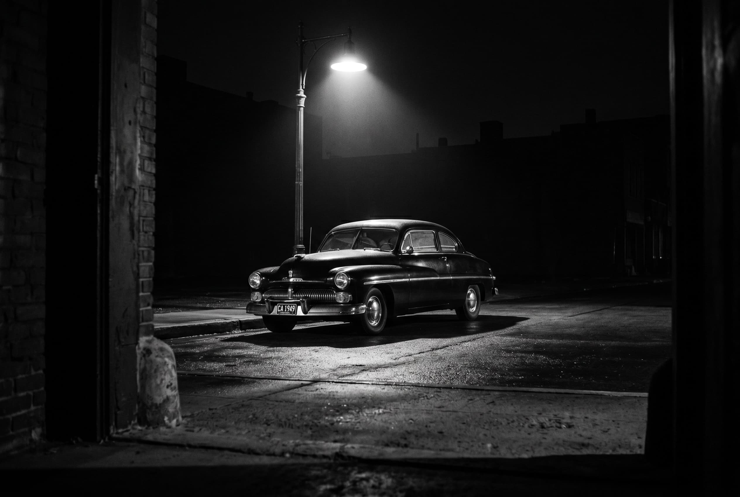 The car as moral presence – noir street scene Black-and-white night photograph of a 1949 Mercury coupe parked under a streetlamp on an empty street