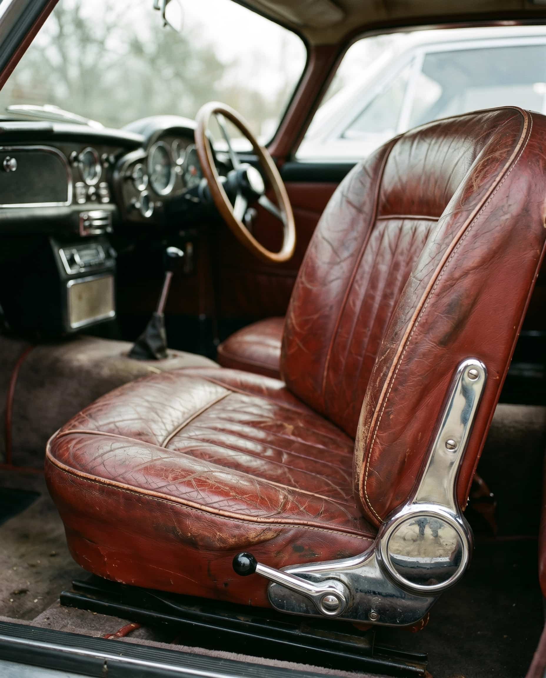 The beauty of gradual wear – aged leather driver's seat Worn but intact leather driver's seat in an older car, creased at the bolsters from years of use, soft natural light