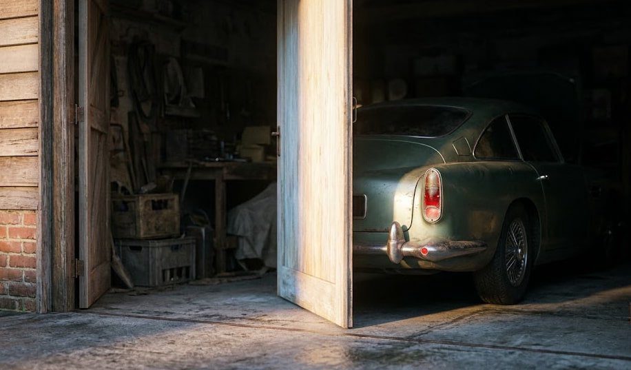 Rear haunch of an Aston Martin DB car half-visible in a dim garage at dawn