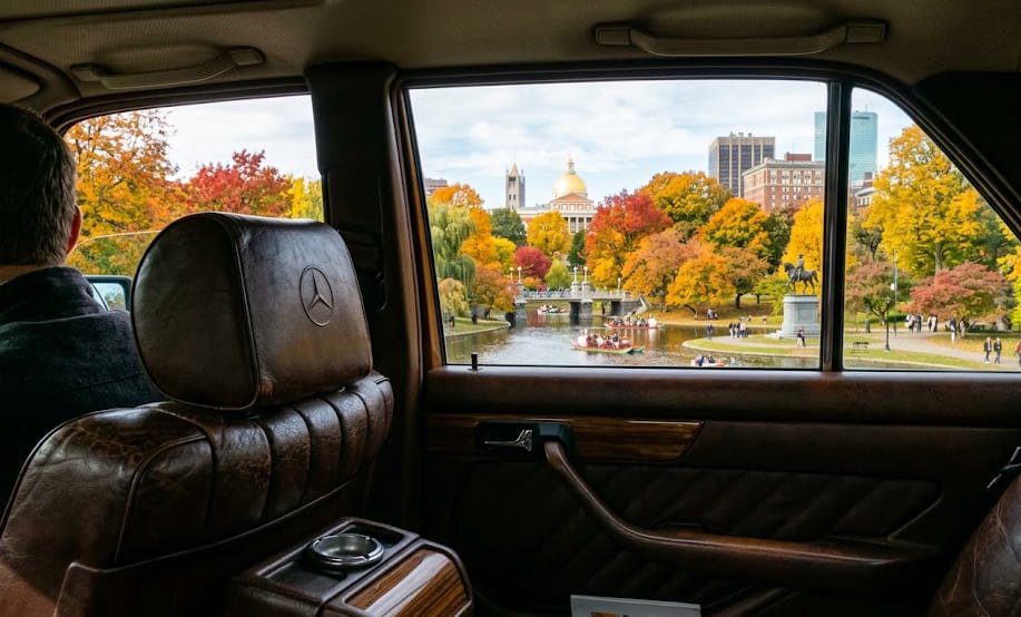 View from rear seat of a Mercedes W126 through clear glass toward Boston Public Garden in autumn