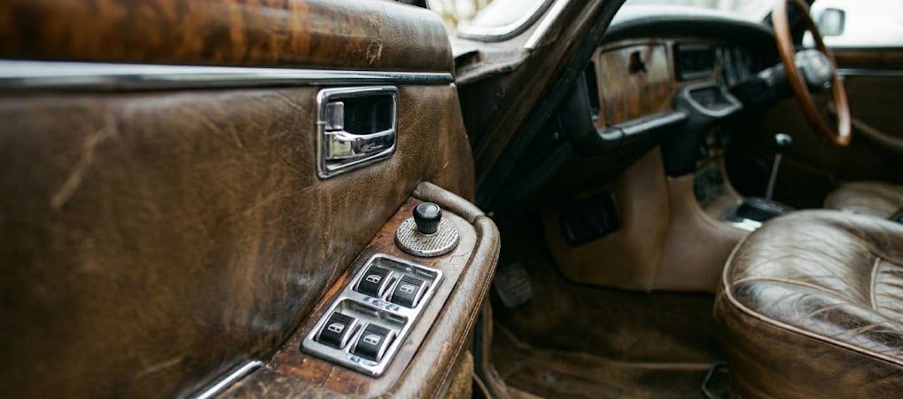 Close detail of worn leather, chrome window switches and manual crank in a Mercedes W123